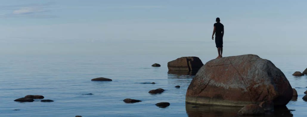 A man standing on a rock looking into the sea, thinking of the challenges of returning to work after mental health treatment.