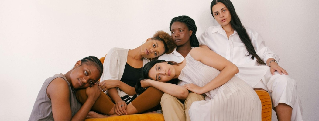 Embraced women dealing with trauma and depression sitting on an orange couch. 